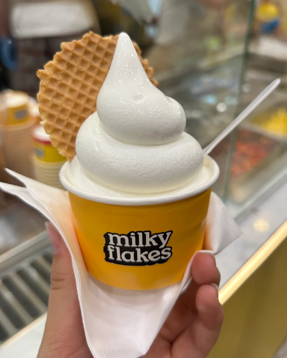 Hokkaido milk soft serve in a yellow milky flakes cup with a waffle cookie, held at the counter.