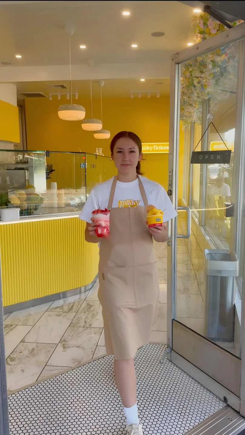 A team member walking out the door holding a strawberry milky flake and an alphonso mango soft scoop.